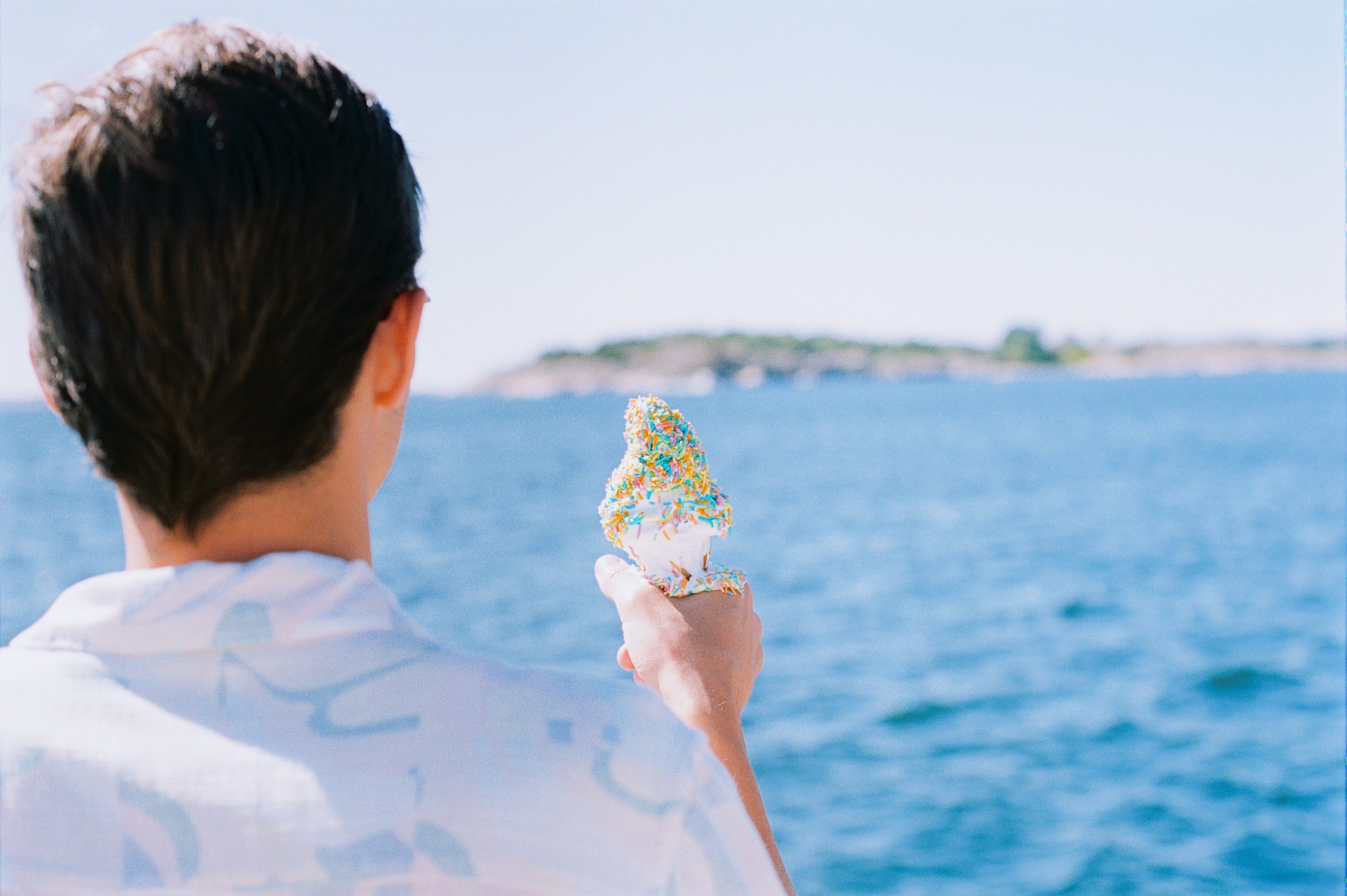 A person by the fjord in Hvitsten holding a soft-serve ice cream covered in rainbow sprinkles.