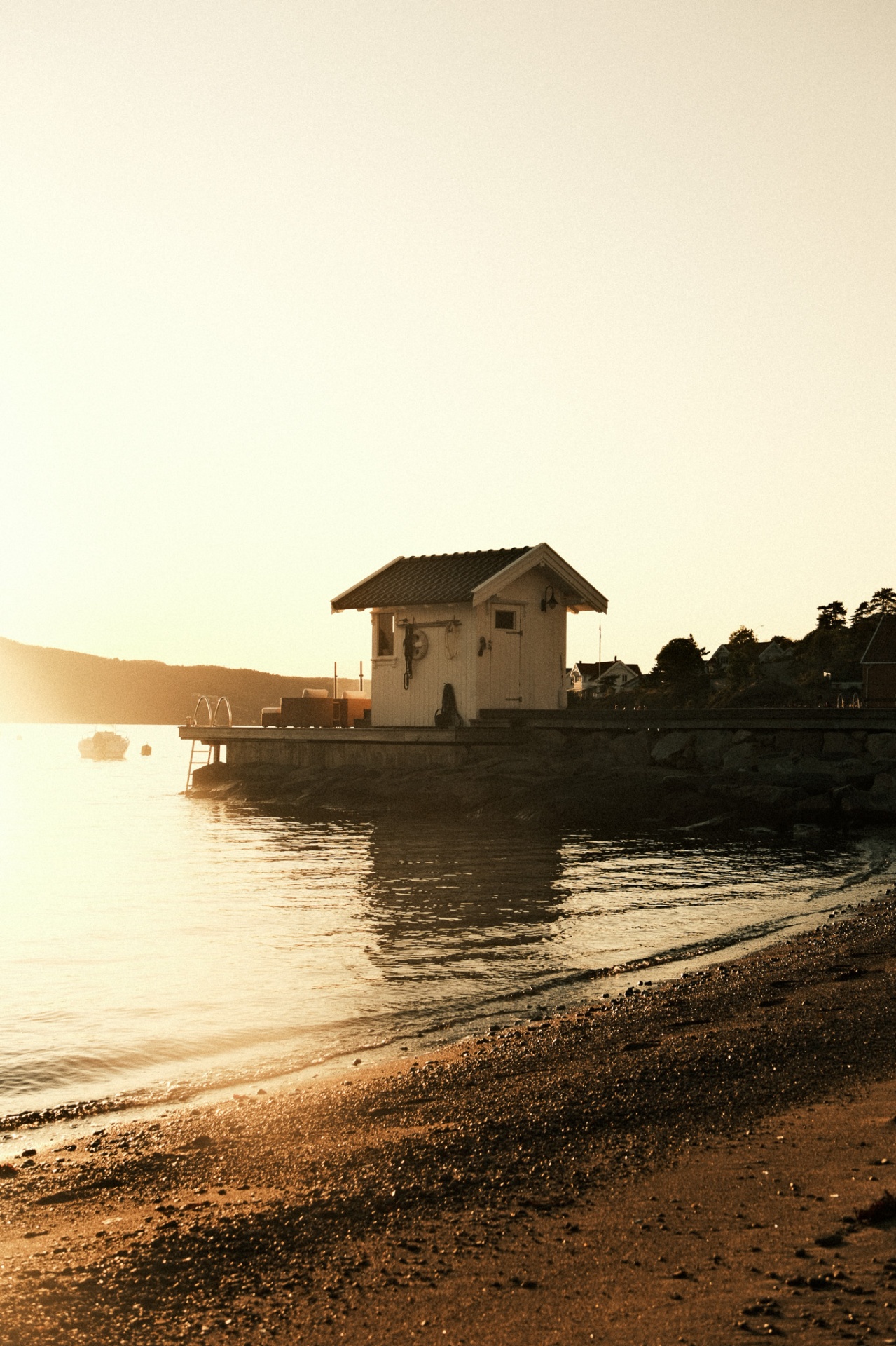 Sjøboden, a small white sea shed at the edge of the fjord in Hvitsten, Norway, glowing in evening light.