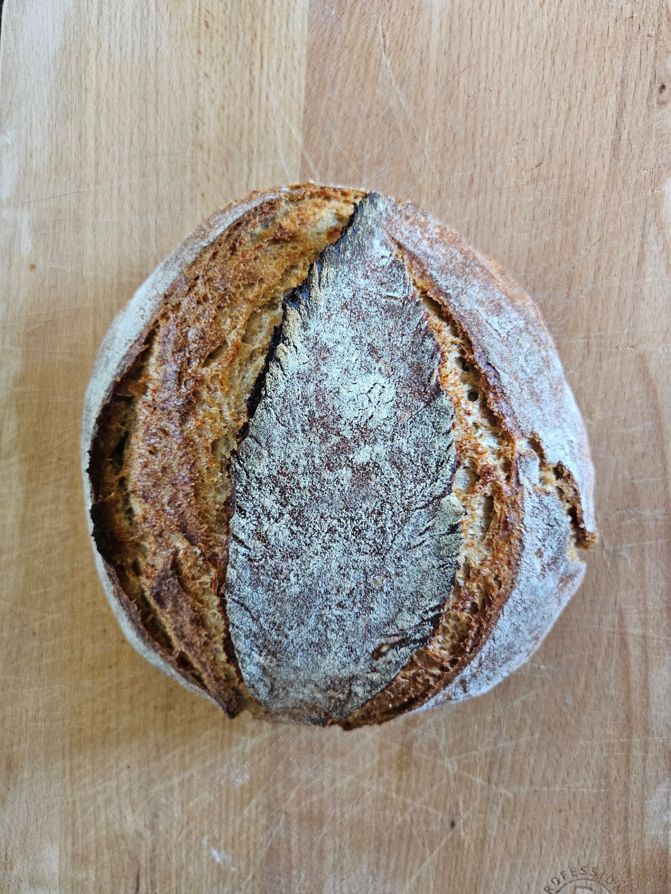 A round, dusted sourdough loaf with a deep dark ear, resting on a worn wooden board.